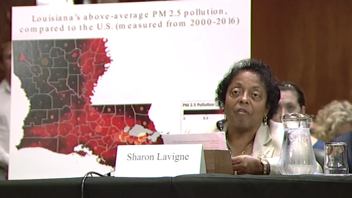 Sharon Lavine sits at a podium with a map of Louisiana behind her