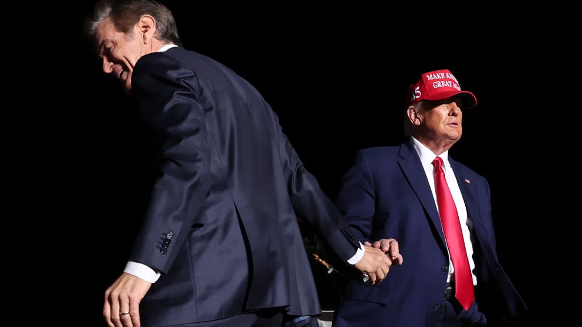 Dr. Mehmet Oz shakes hands with Donald Trump on stage against dark background