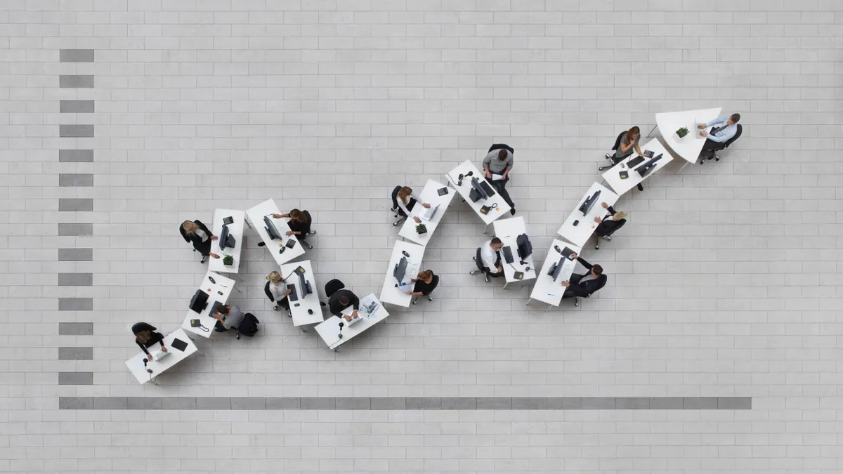 business graph in birdsview, office seen from above with emploees sitting at their work stations in a formation shaped like a graph, showing growth