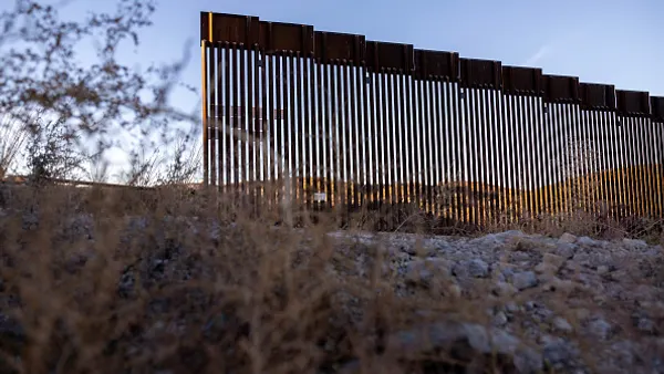a brown border wall rises in the desert