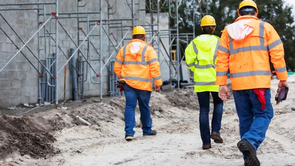 A group of construction workers on a jobsite walk away, their backs toward the camera.