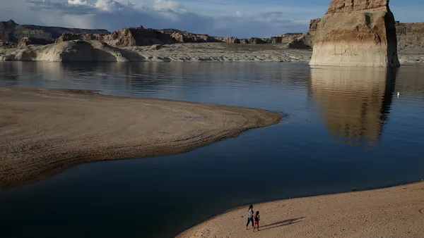 People walk on a beach that used to be the bottom of Lake Powell amid big rock formations.