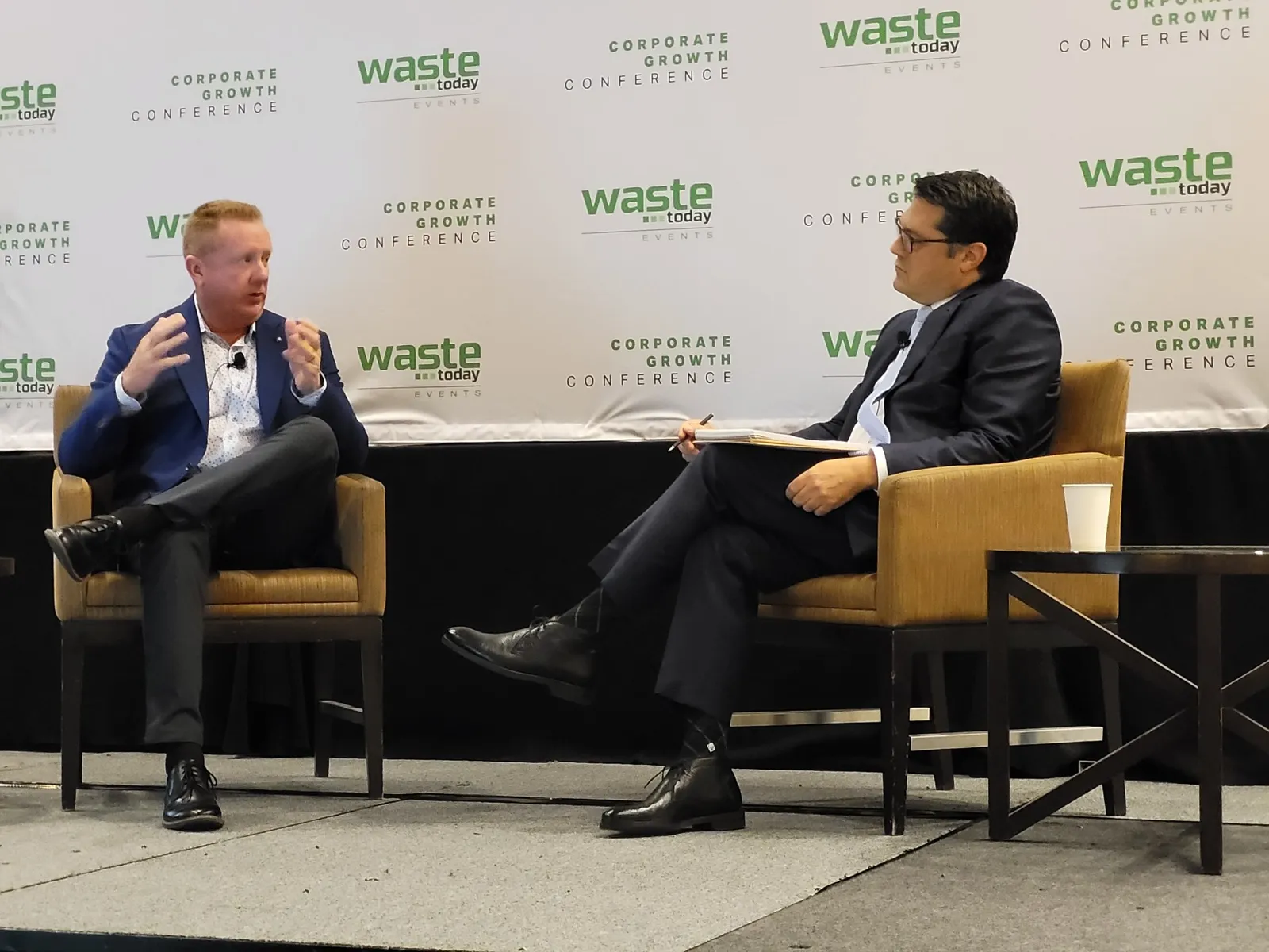 Two people seated in chairs on a stage, Waste Connections CEO Ron Mittelstaedt on the left