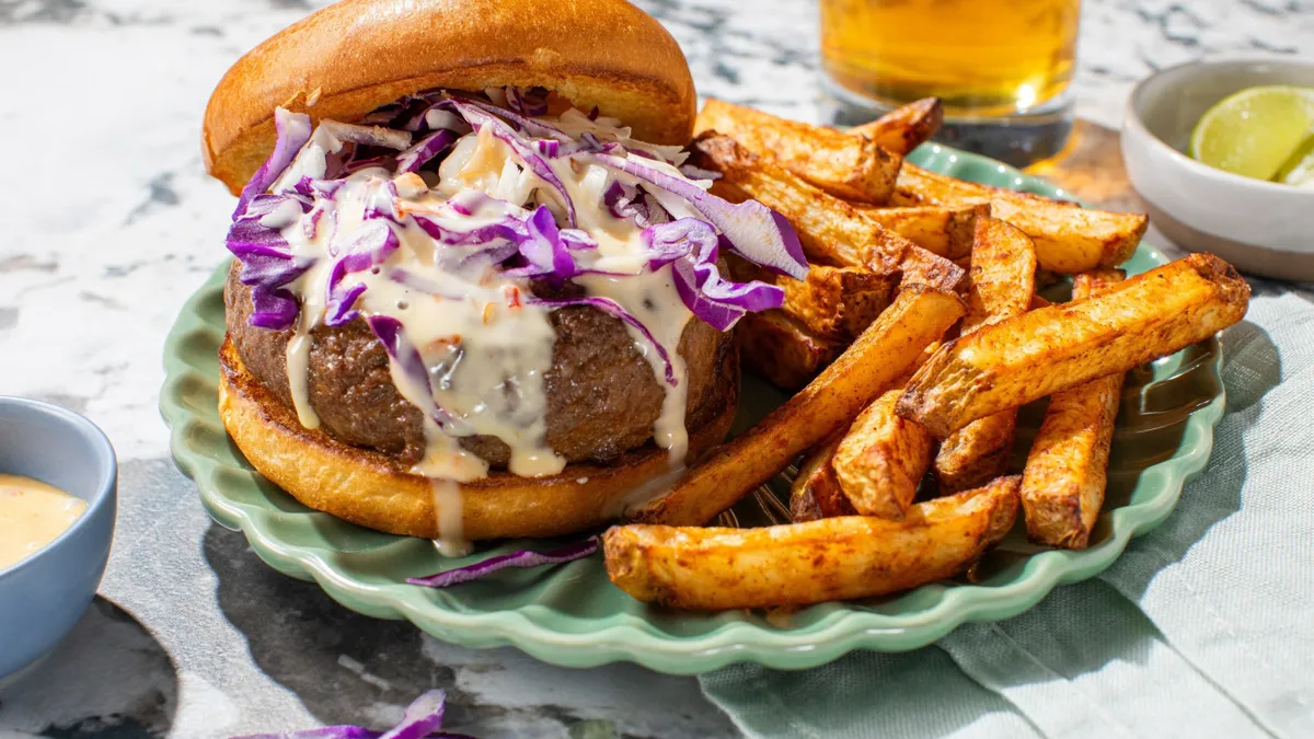 Beef burger with coleslaw and fries on a green plate