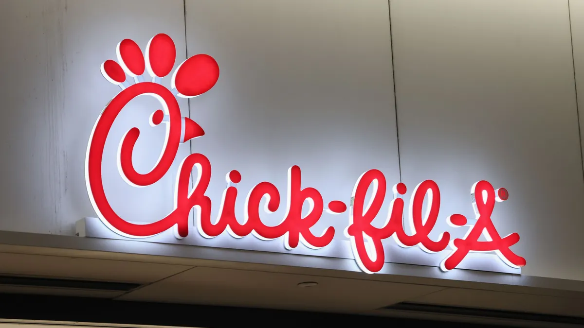 A red sign that says Chick-fil-A on a white wall.