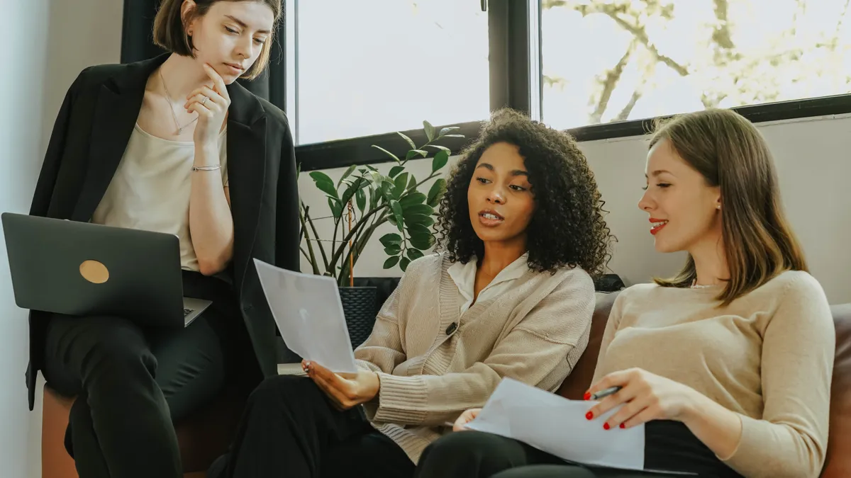 A woman of color sits against an office window and teaches her colleagues