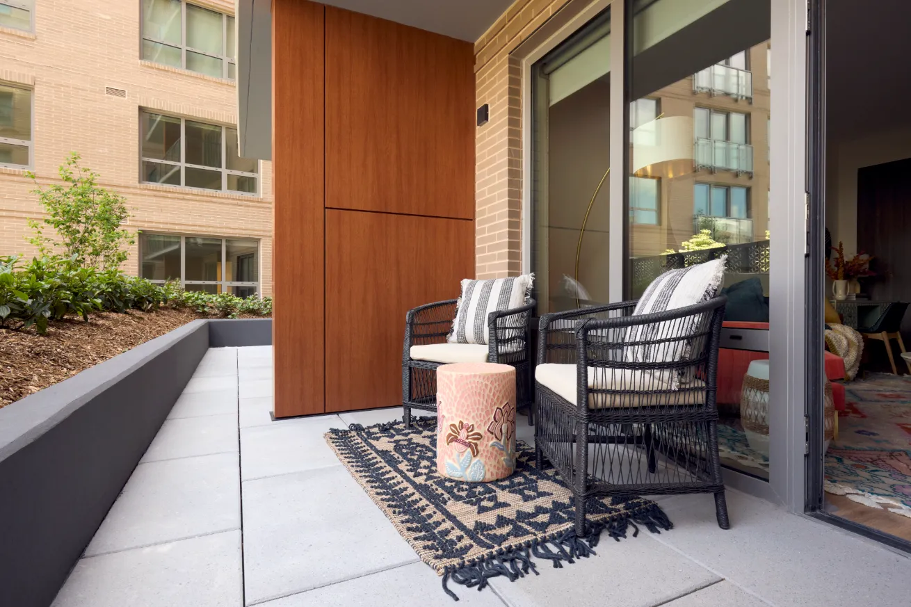 A terrace with two chairs and a glass sliding door leading into a room.