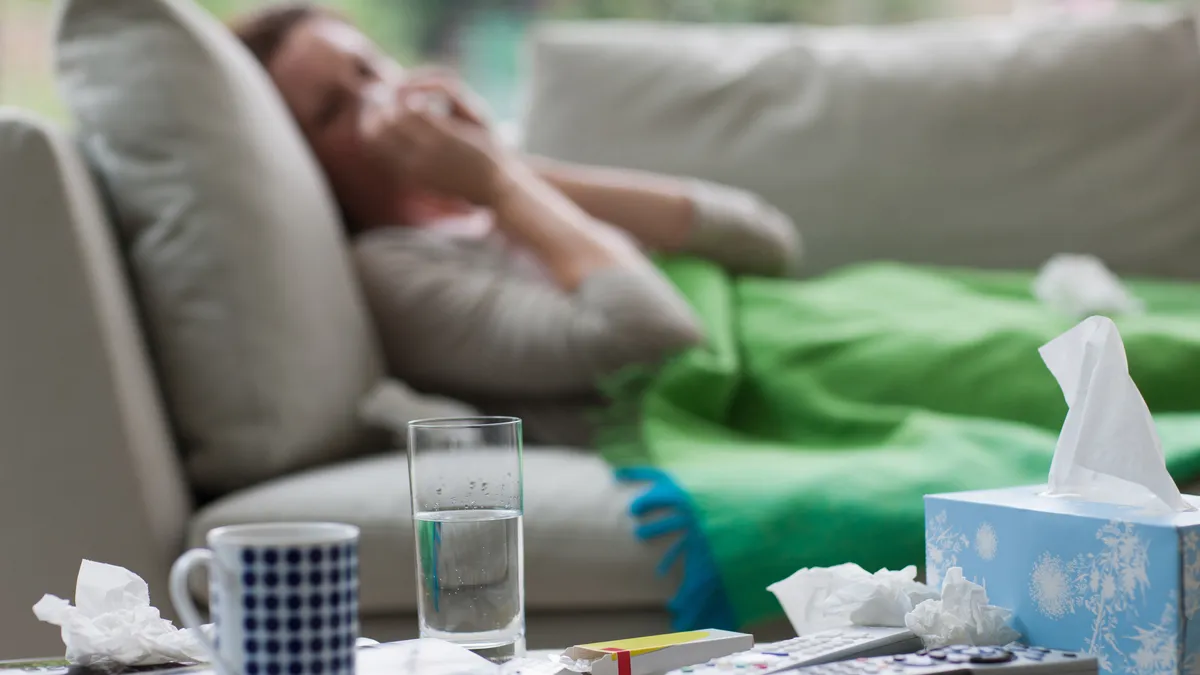 A person with an upper respiratory illness lays on the couch while resting at home.