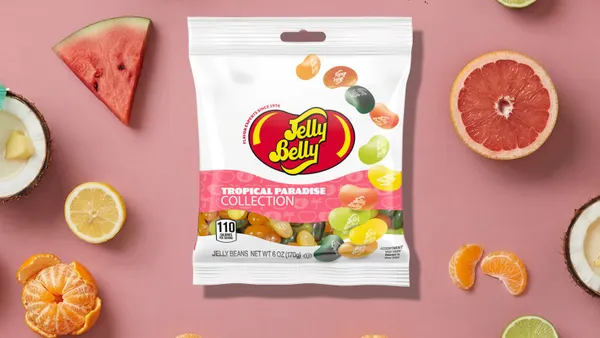 A bag of Jelly Belly candy on a pink background surrounding by whole fruit.