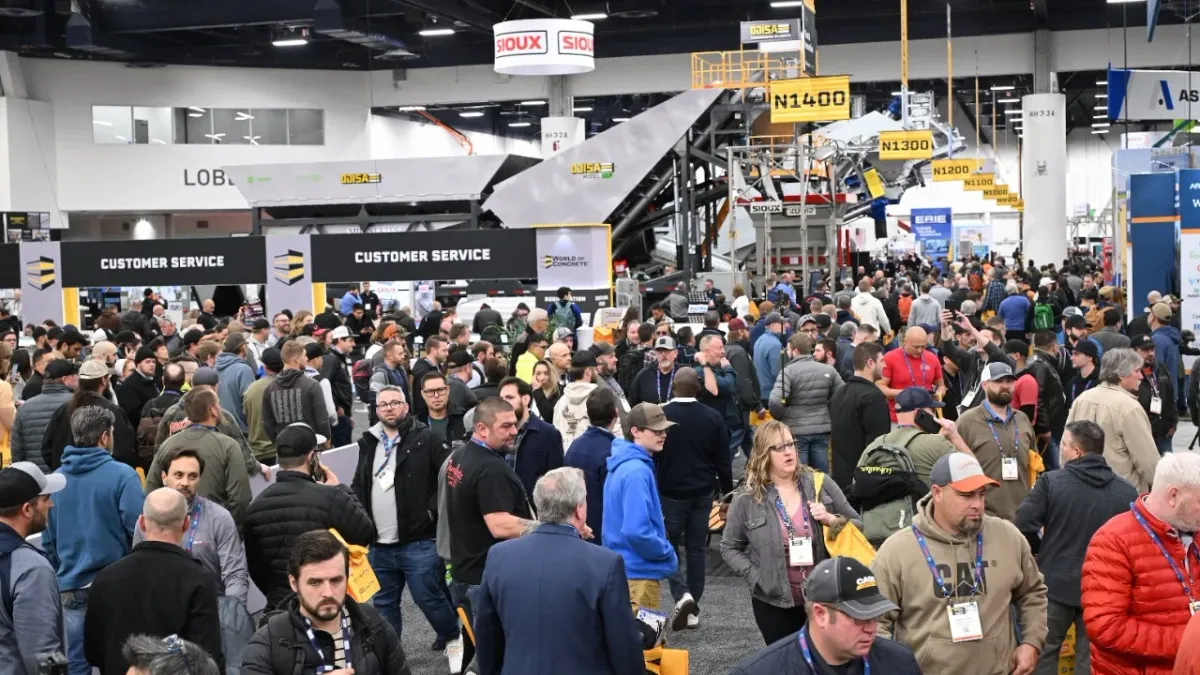 People mill about an exhibition hall with a variety of construction-related exhibits around them.