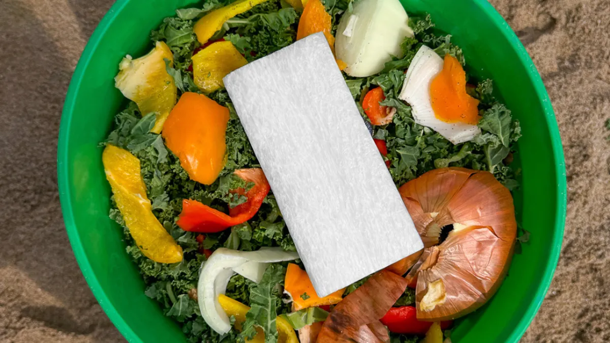 A piece of foam placed on top of food scraps in a green compost bowl.