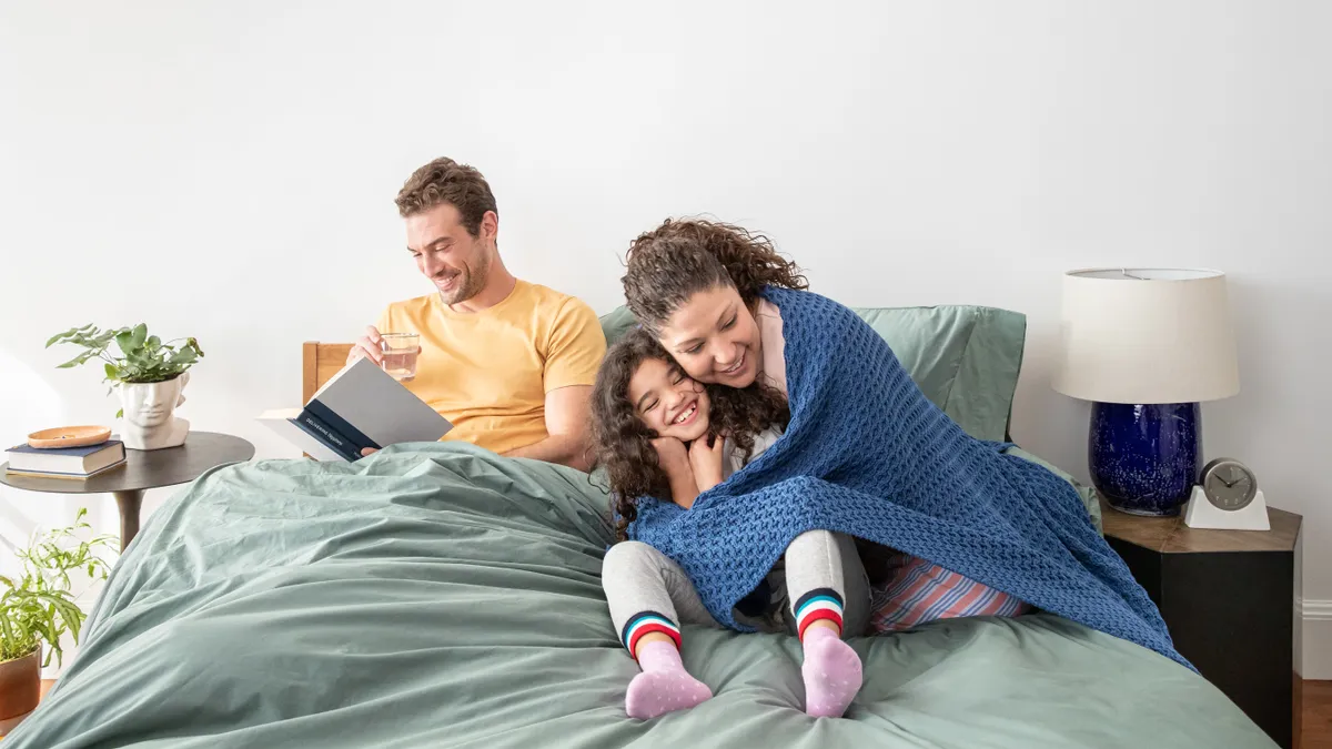 A family lounges on a bed with sage-green covers.