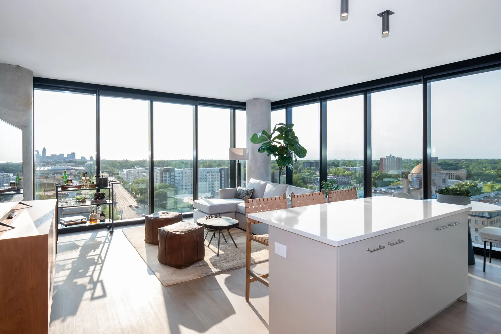 A kitchen space full of white furniture and floor-to-ceiling windows overlooking a cityscape.