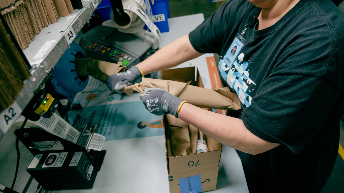 An Amazon employee's hands tear off kraft paper to use as protective filler in an Amazon box.