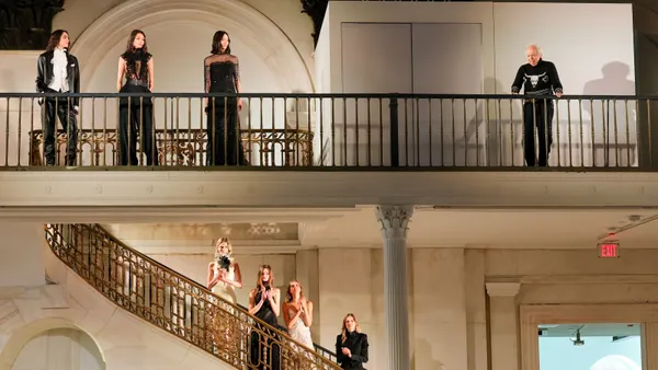 Models stand on a filigree staircase and applaud as more models and designer Ralph Lauren looks on from a balcony.