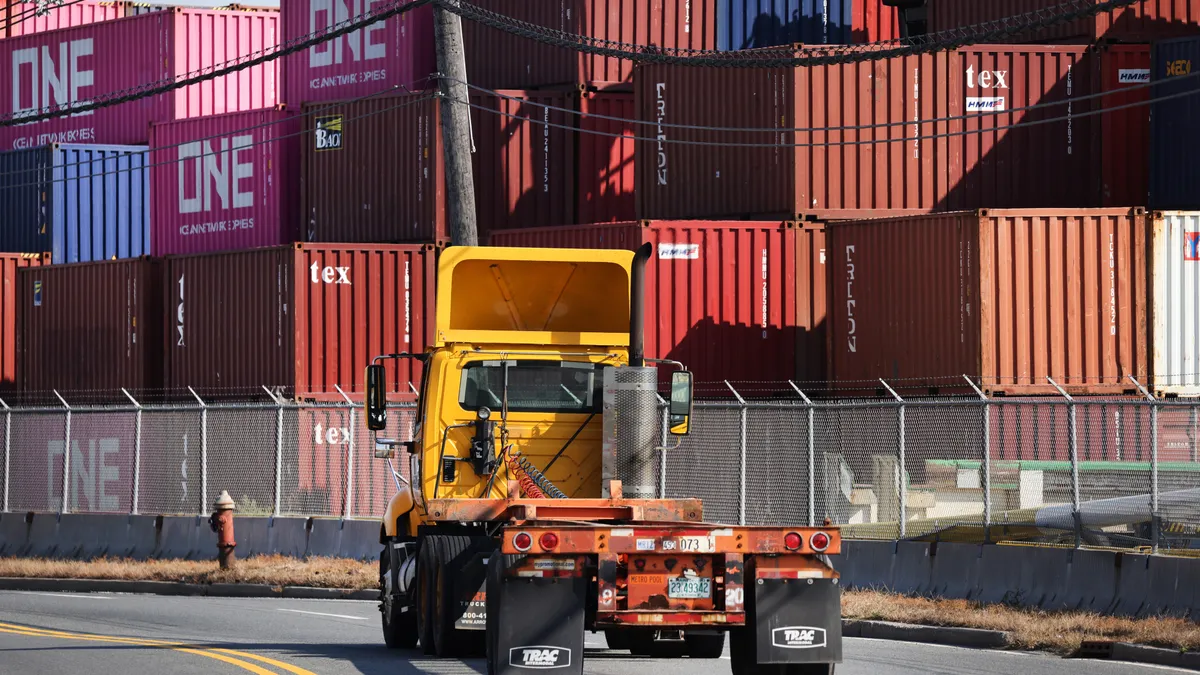 Shipping containers are seen in the background with a truck cab in foreground