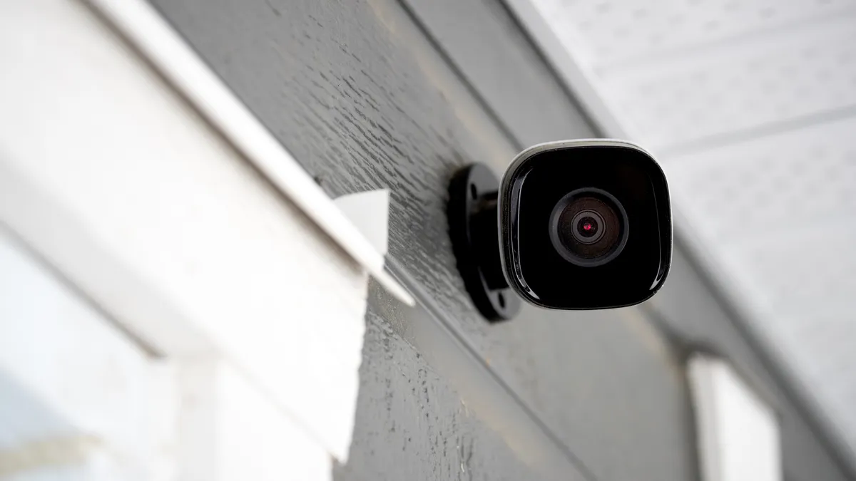 A security camera on the side of a home with gray siding.