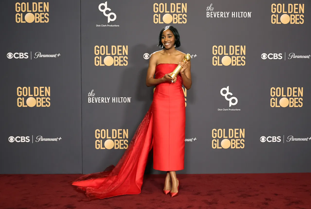 Ayo Edebiri wears a red gown and poses with a Golden Globe award.