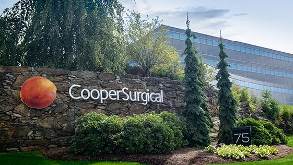 A sign says "CooperSurgical" in front of some trees with an office building in the background.