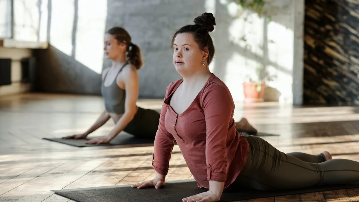 Two people, including a person with Down syndrome, do yoga together in a studio