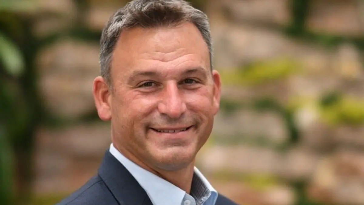 A headshot shows Kevin Thornal against a blurred background of a stone wall with green foliage.