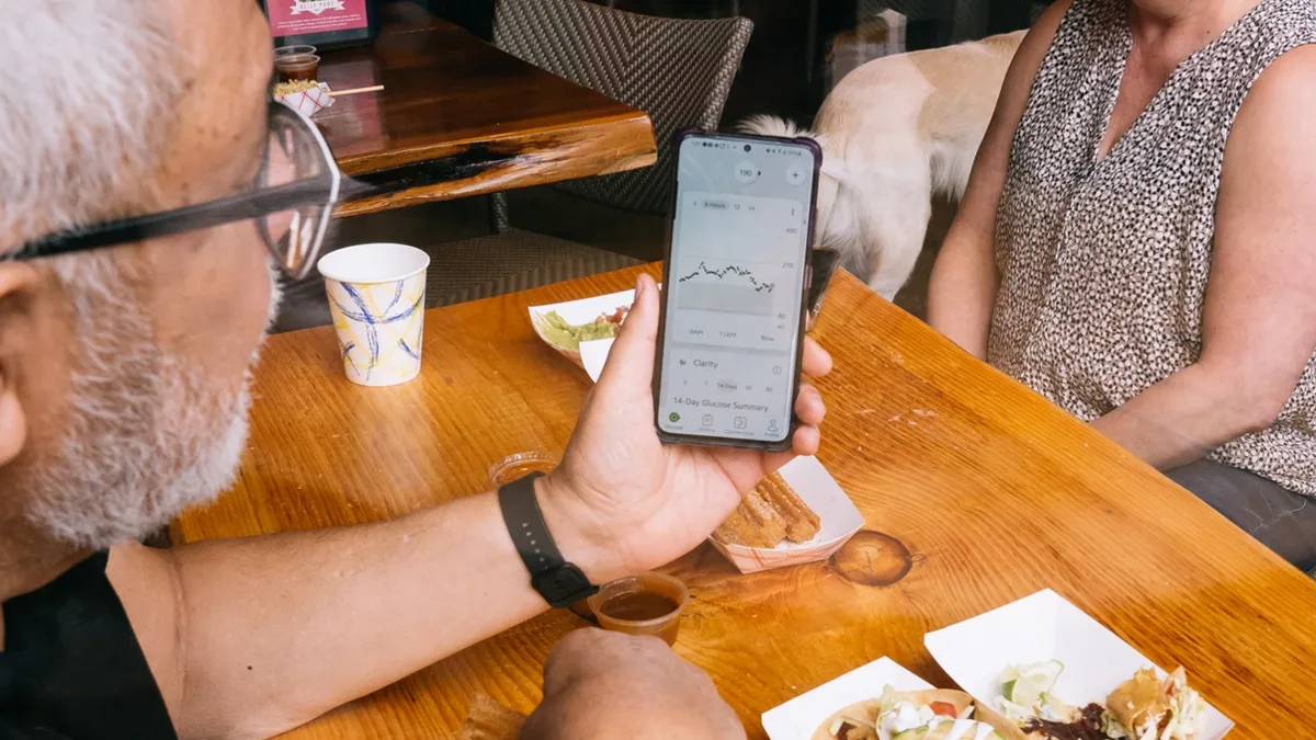 A picture of two people sitting at a table looking at a smart phone.