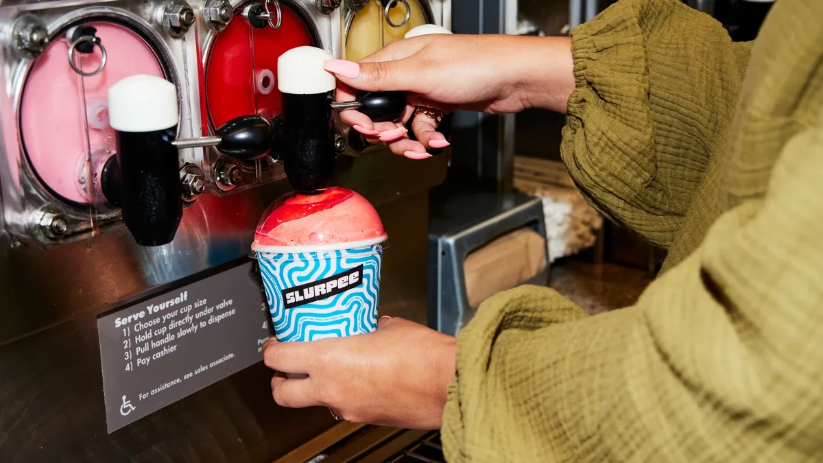 A photo of a person dispensing a Slurpee at a 7-Eleven store.