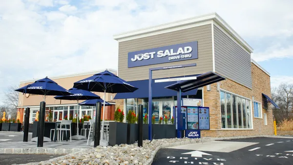 A building with a drive-thru that is blue and white. Signage says Just Salad.