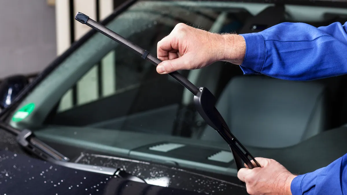 A hand pulls up a windshield wiper on a car to check it