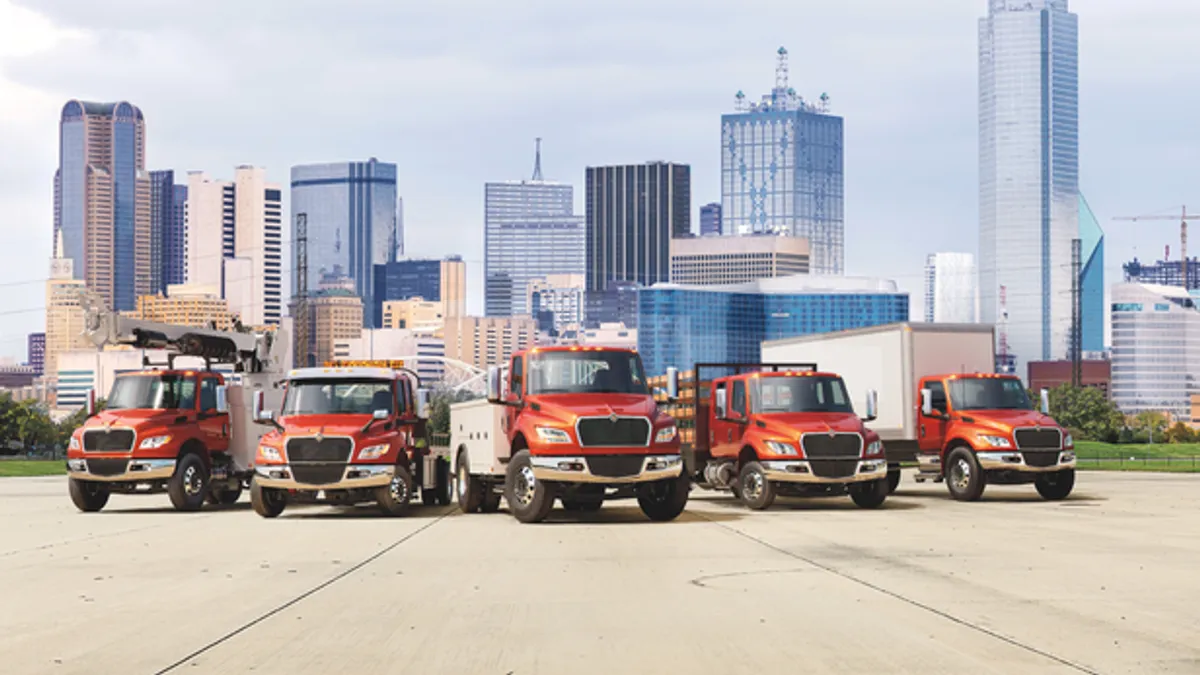 A group of 5 International MV trucks parked in front of a backdrop of city skyscrapers.