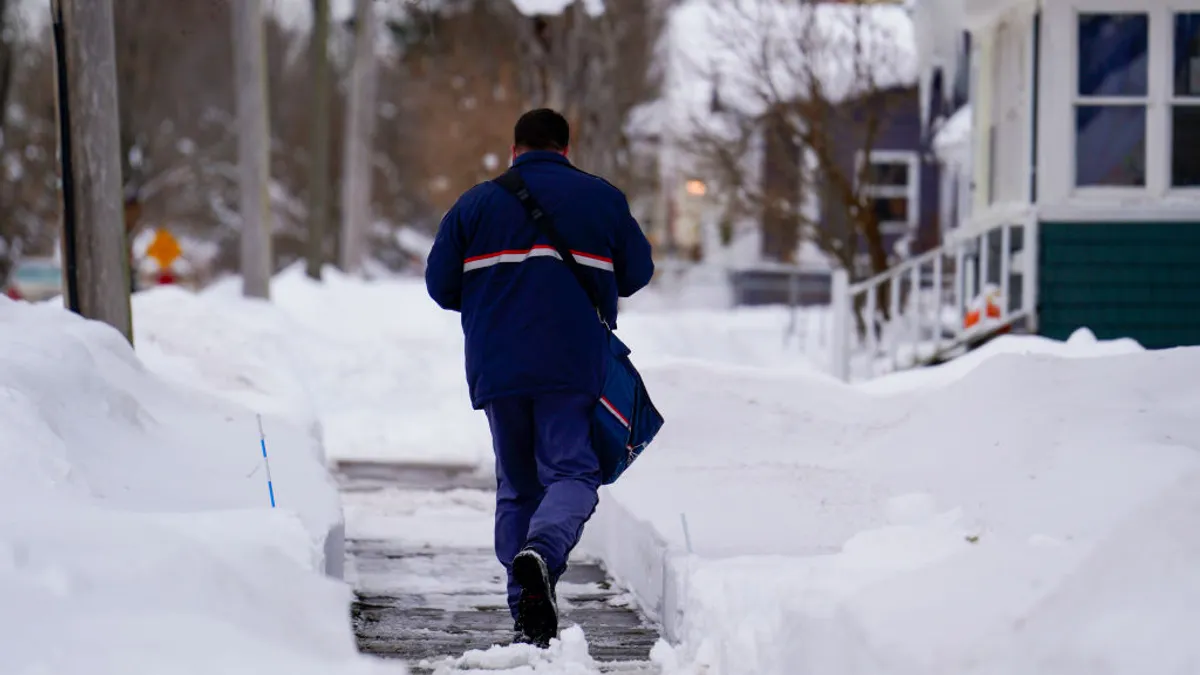 A person walks on a sidewalk in a snow-filled neighborhood.