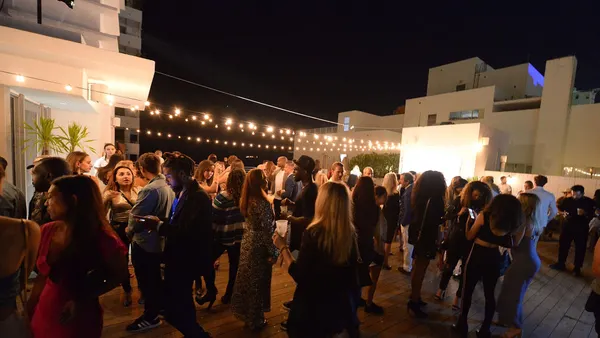 A crowd of people on a rooftop lit by string lights.