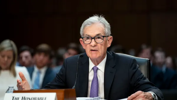 Federal Reserve Chair Jerome Powell, wearing a suit and tie, addresses senators with a microphone in front of him and people behind him.