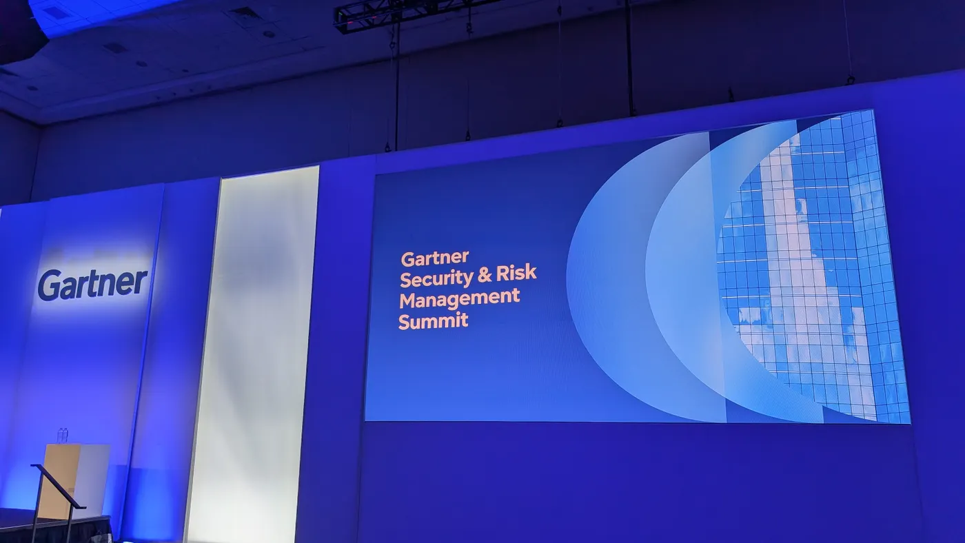 The Gartner logo is displayed on a blue lit-up wall next to a screen that displays the words “Gartner Security & Risk Management Summit”