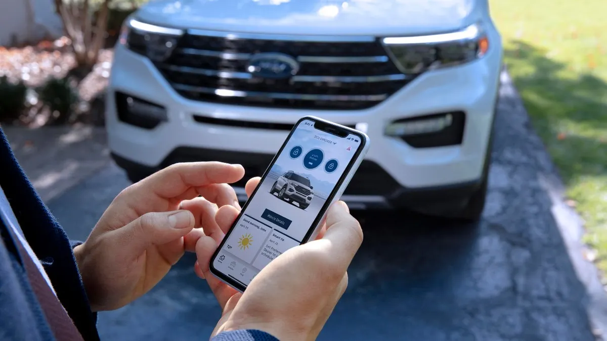 A person viewing the FordPass app on a smartphone with a white 2023 Ford Explorer SUV in the background.