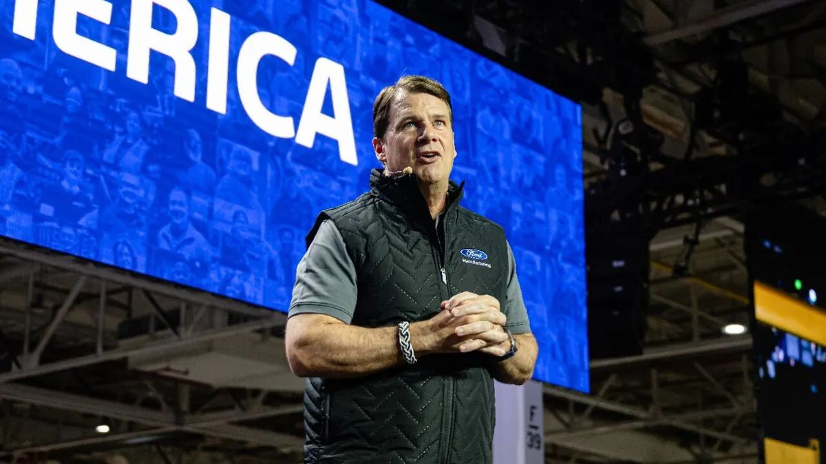 Ford CEO Jim Farley speaking to workers at the automaker's Kentucky Truck Plant in April 2025 with a large blue display screen behind him.