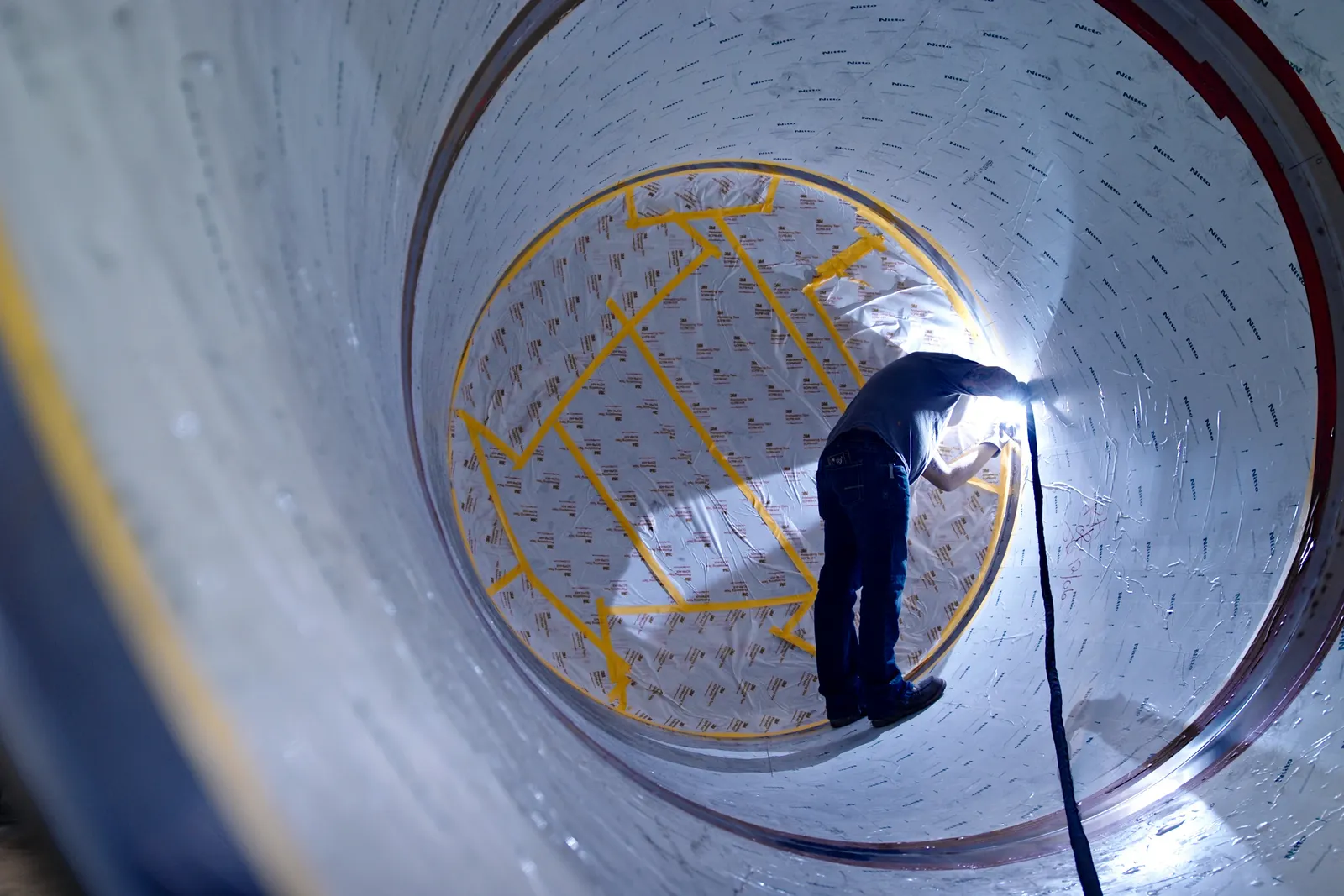 A person welds inside a large oval container.