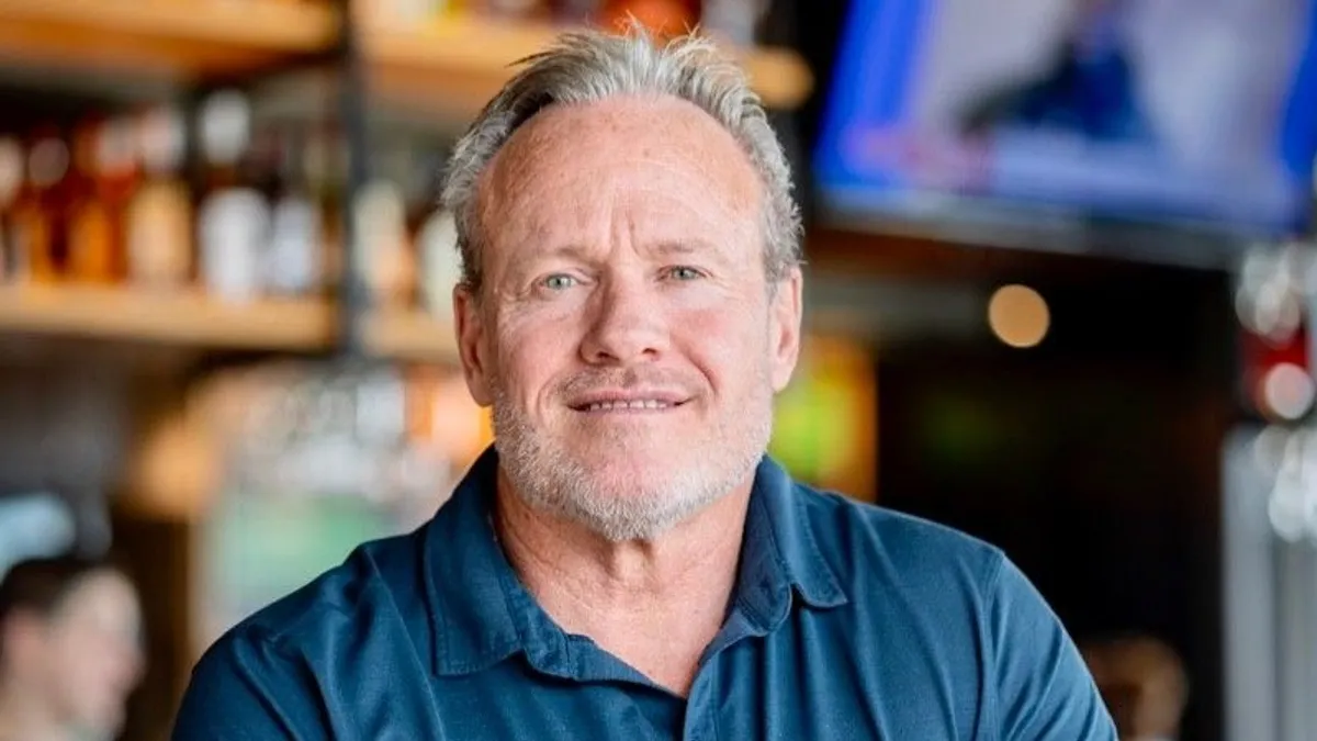 An image of a man wearing a blue shirt with arms crossed.