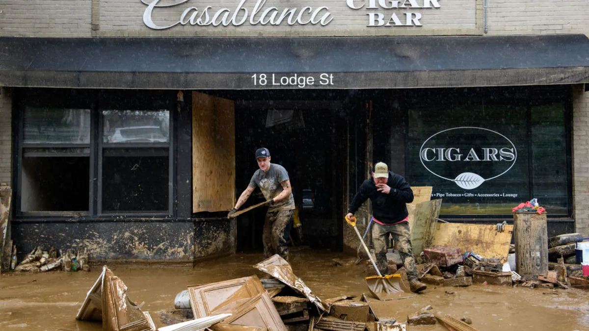 Building debris sits in mud outside a building that reads "Casablanca Cigar Bar 18 Lodge St." Two people carry items out of the building.