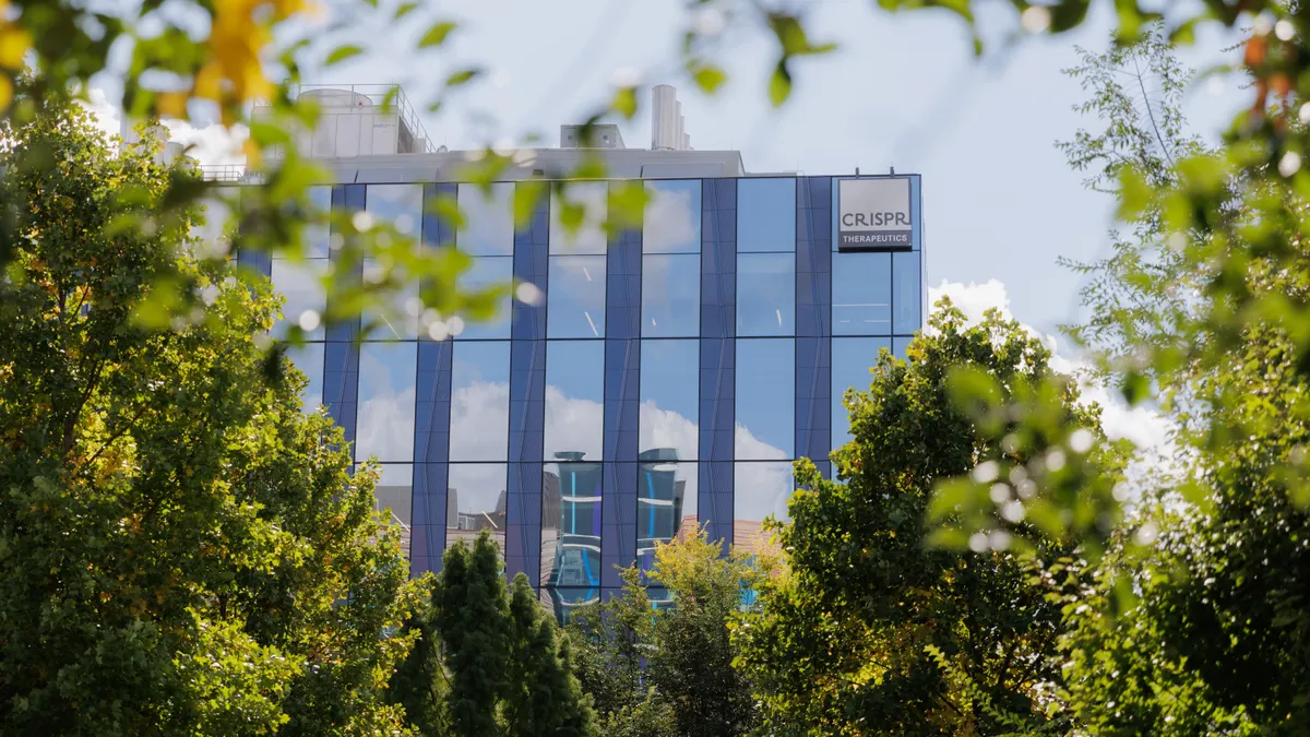 A CRISPR Therapeutics sign is seen on the side of a building viewed through trees.