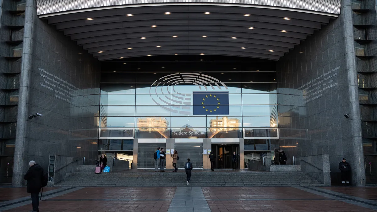 The front doors to the EU parliament are pictured as pedestrians enter and stand around it.