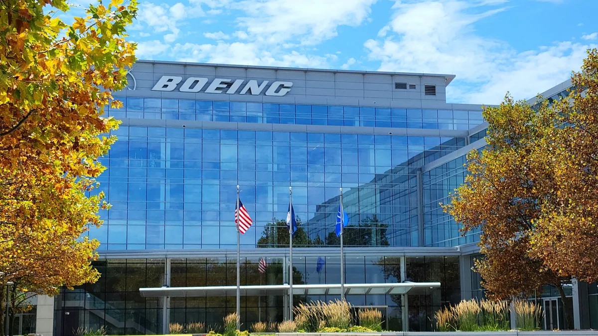 A building with glass windows and the white Boeing logo in between rows of trees.