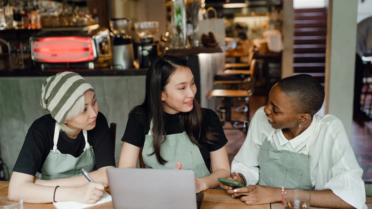 People in a coffee shop sitting at a table talking in front of a laptop