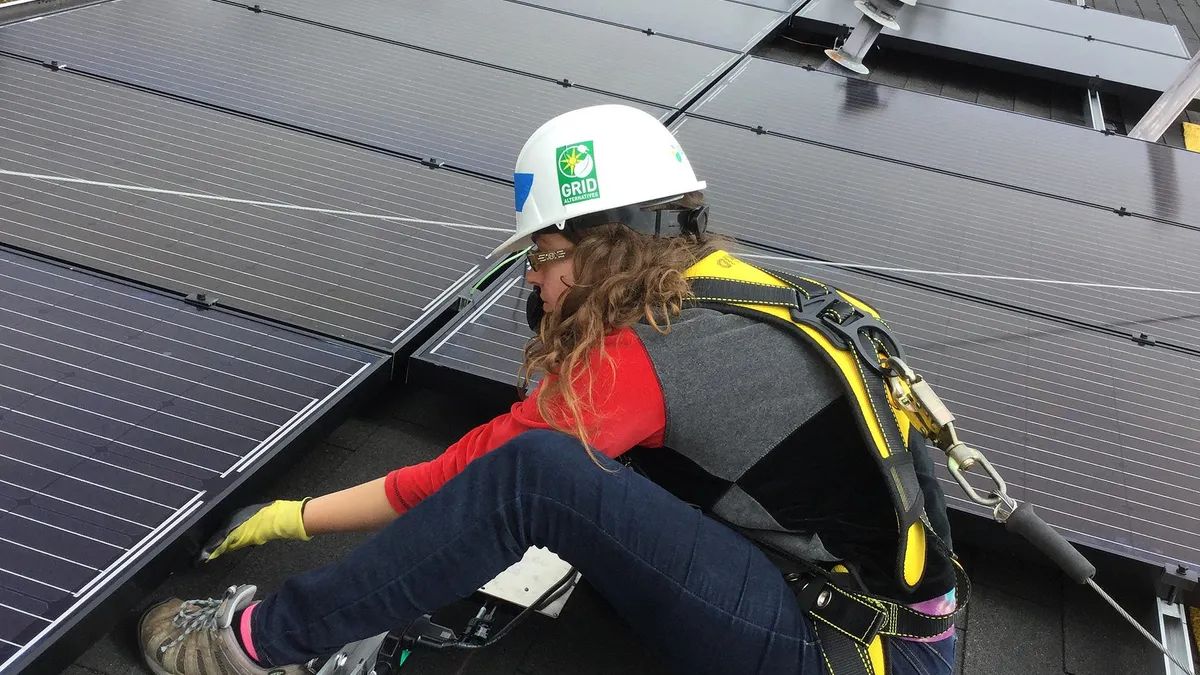 A woman installs solar panels on a roof.