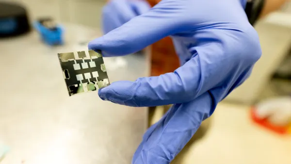 A gloved hand holds a small solar cell.