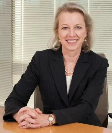 Susan Mayne sits at a desk with drawn blinds behind her.