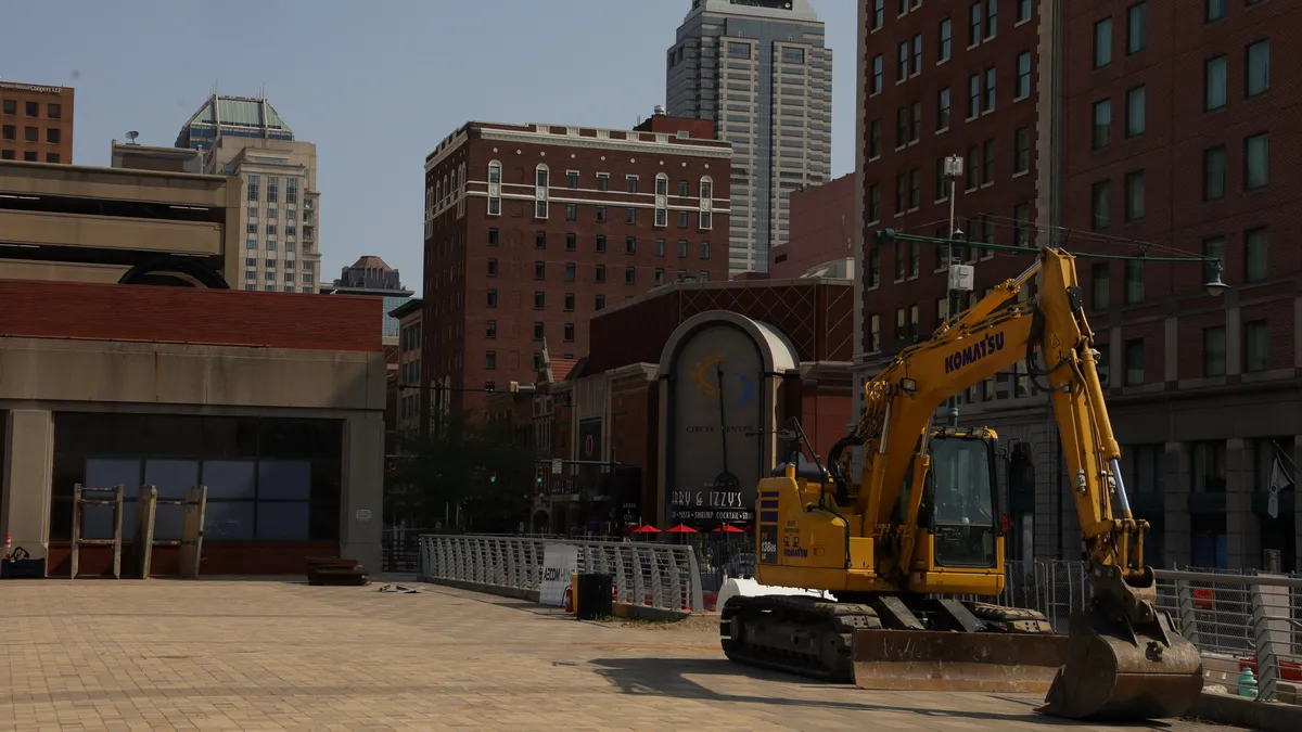 A lone piece of heavy machinery looms on a flat construction site. It's evening, and the ground is paved tile.