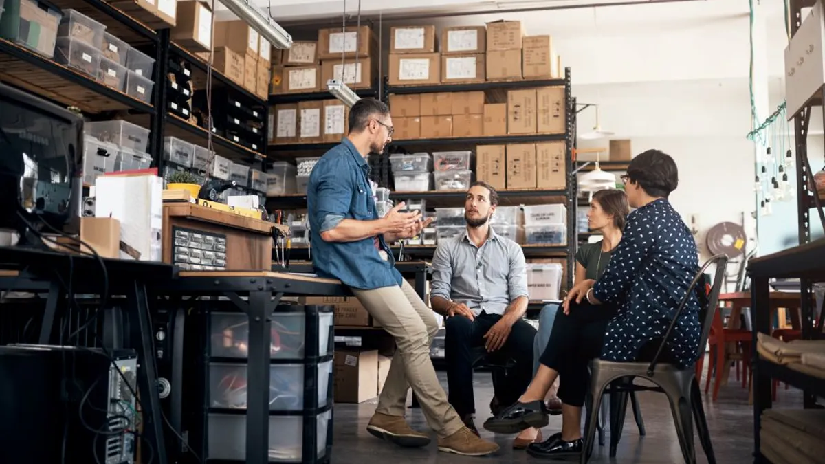 A group of people gathered around a table inside a warehouse, engaged in discussion and collaboration.