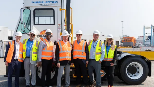 Orange EV and APM Terminals team members stand in front of an electric terminal truck to smile for a photo.