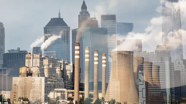 Smoke billowing from smoke stacks in front of skyscrapers.